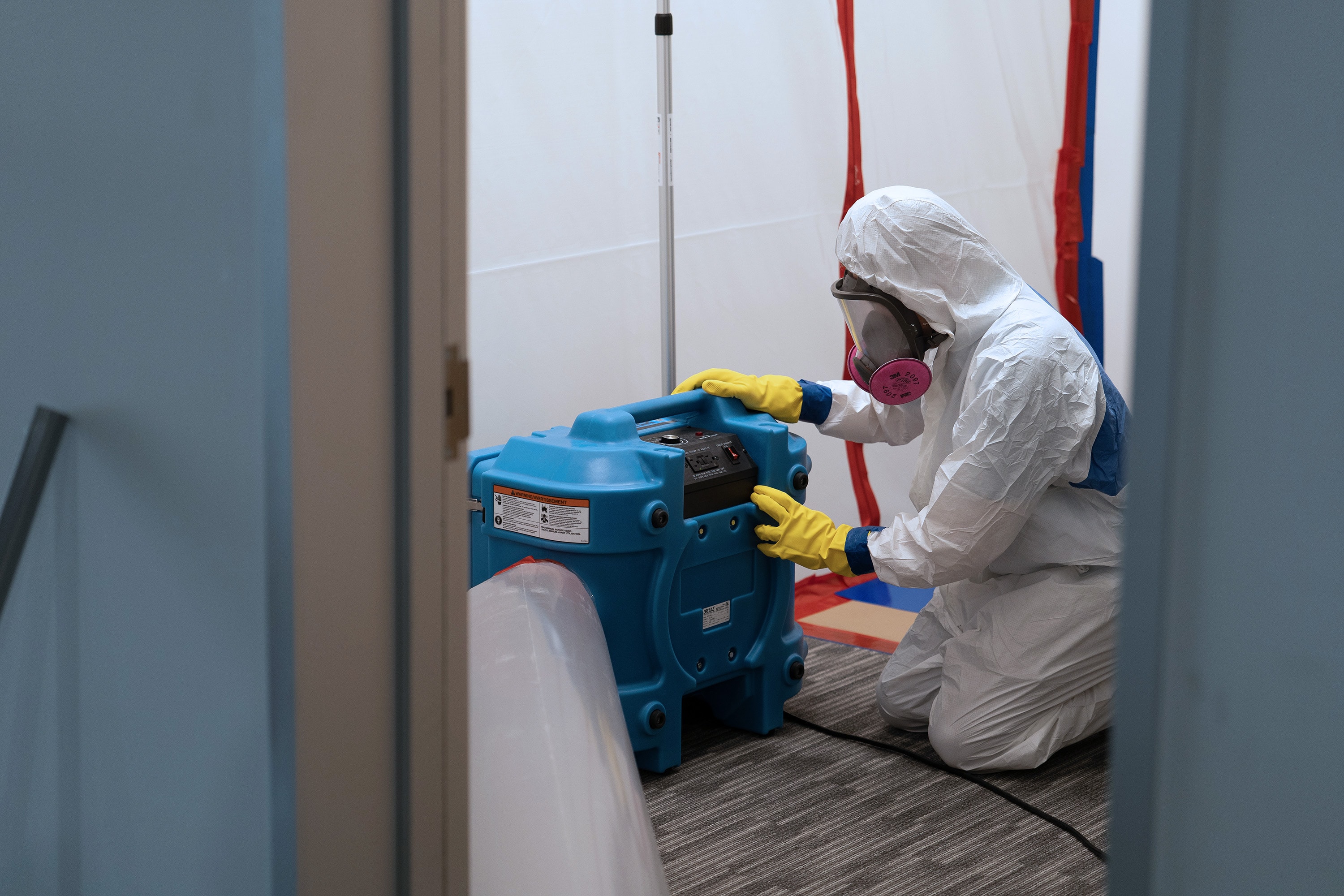 A technician working a HEPA air scrubber in a contained area.