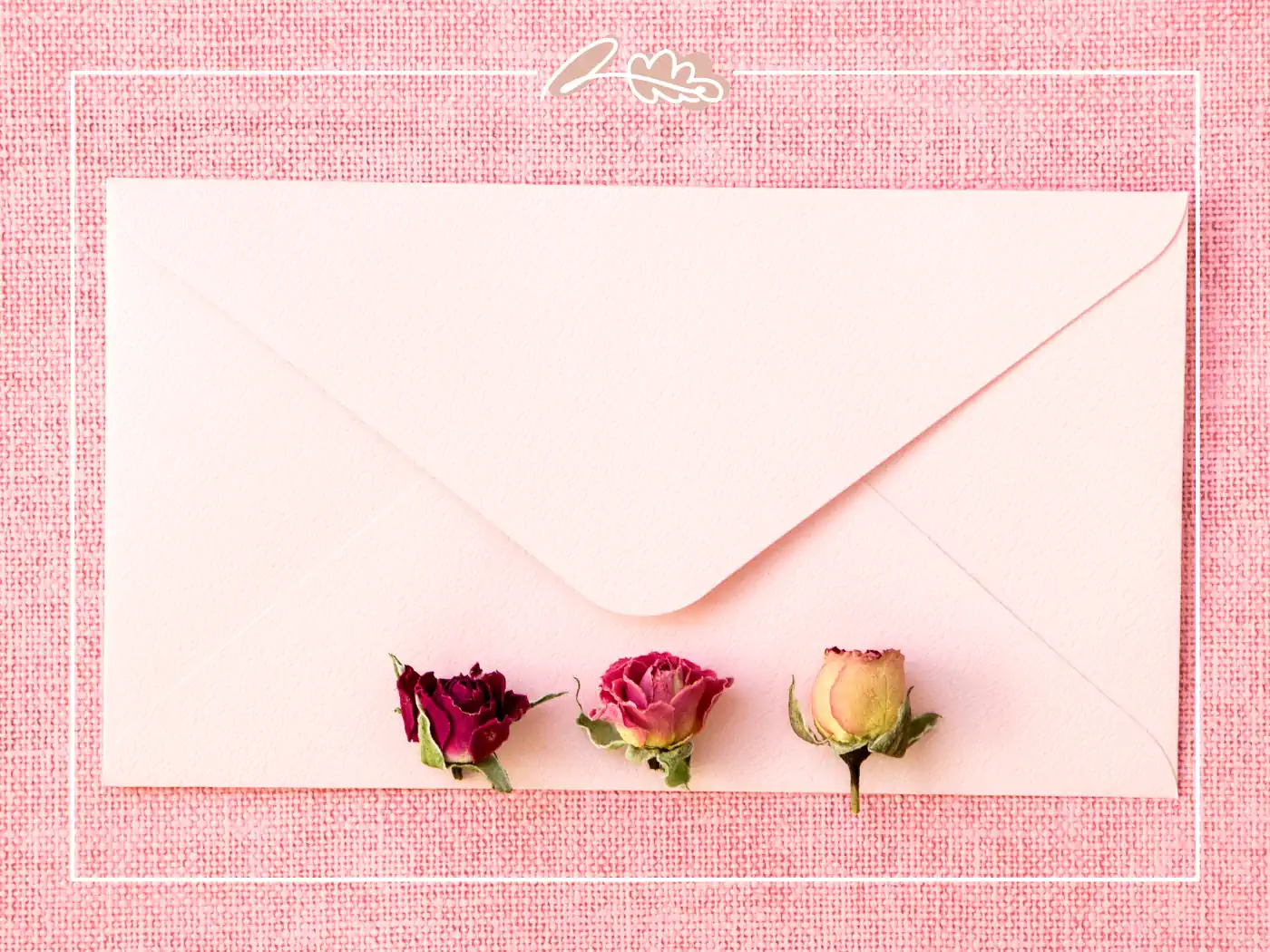 An elegant pale pink envelope adorned with three small dried roses in shades of red, pink, and yellow, set against a pink textured background. Fabulous Flowers and Gifts.