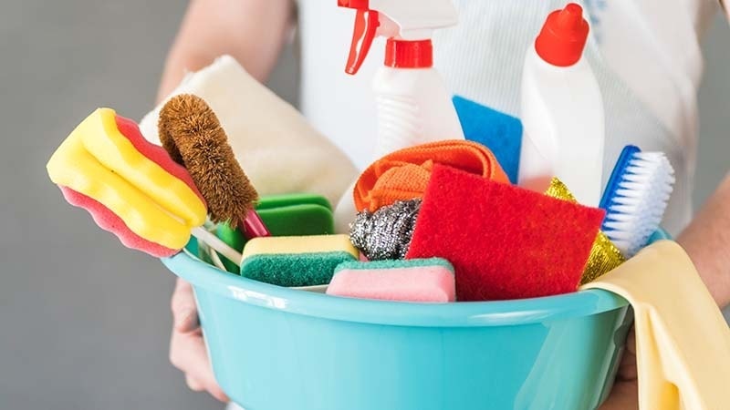 A woman holding a tub full of cleaning supplies