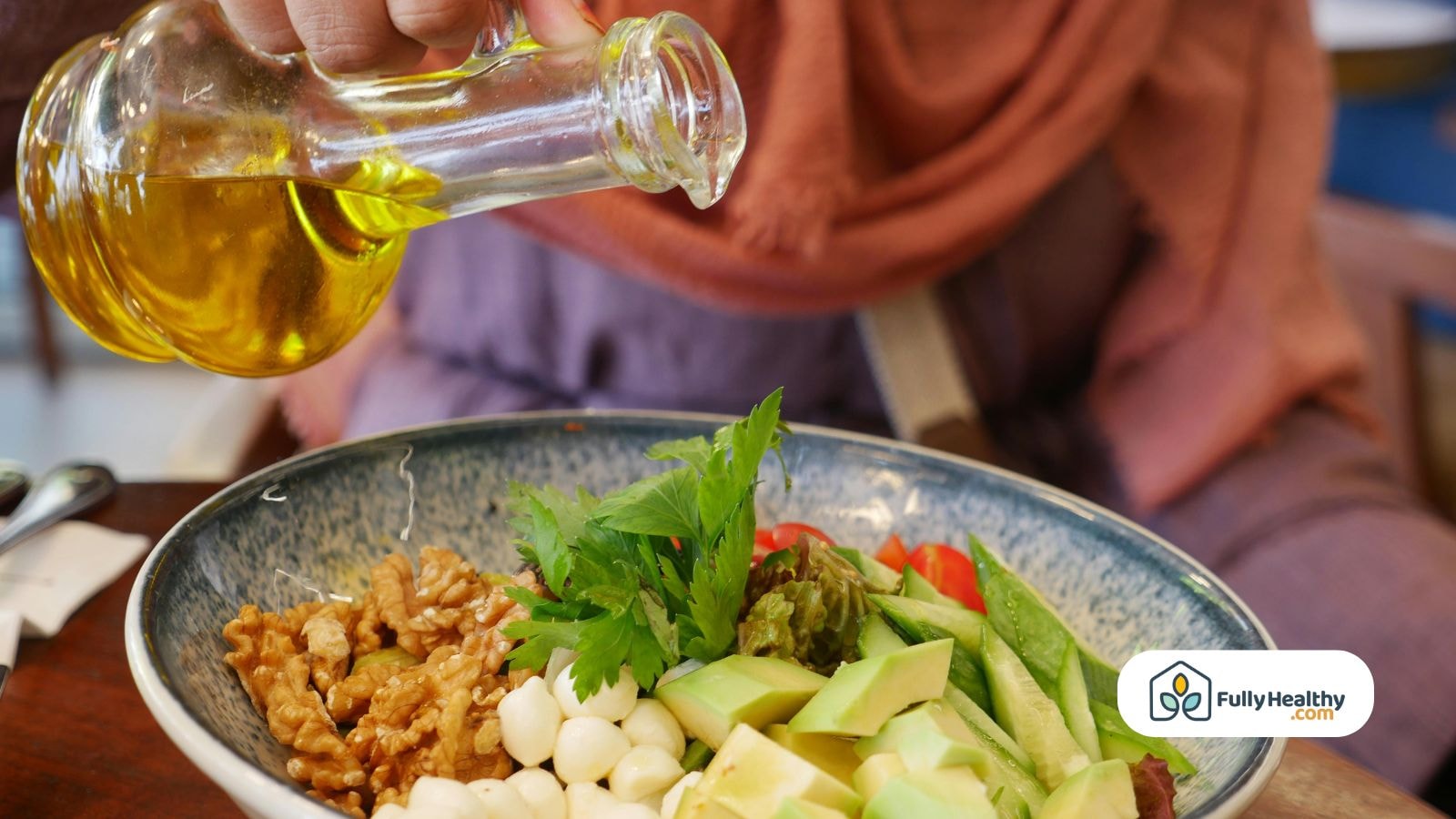 Person pouring olive oil over fresh salad with avocado and walnuts