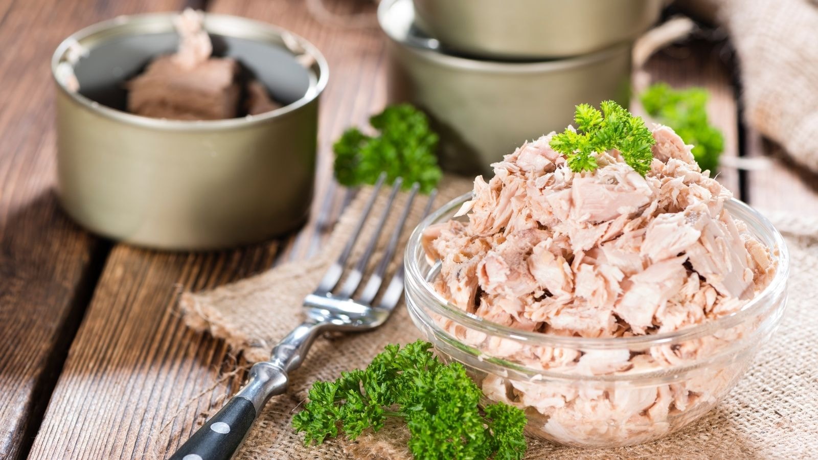 Bowl of flaked canned tuna with parsley and fork on wooden table