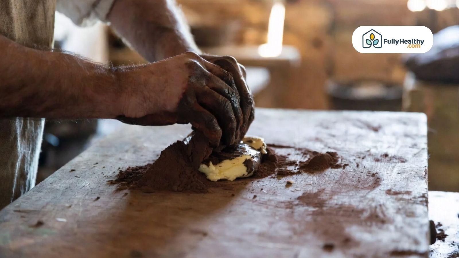 Hands mixing cocoa powder and butter on a wooden surface.