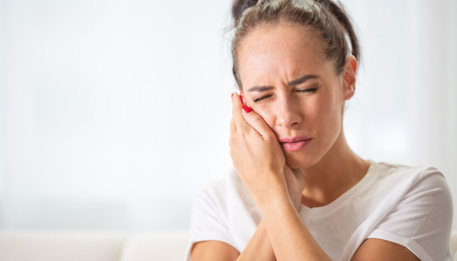 Kvinne holder seg til kinnet – typisk ved tannbyll.