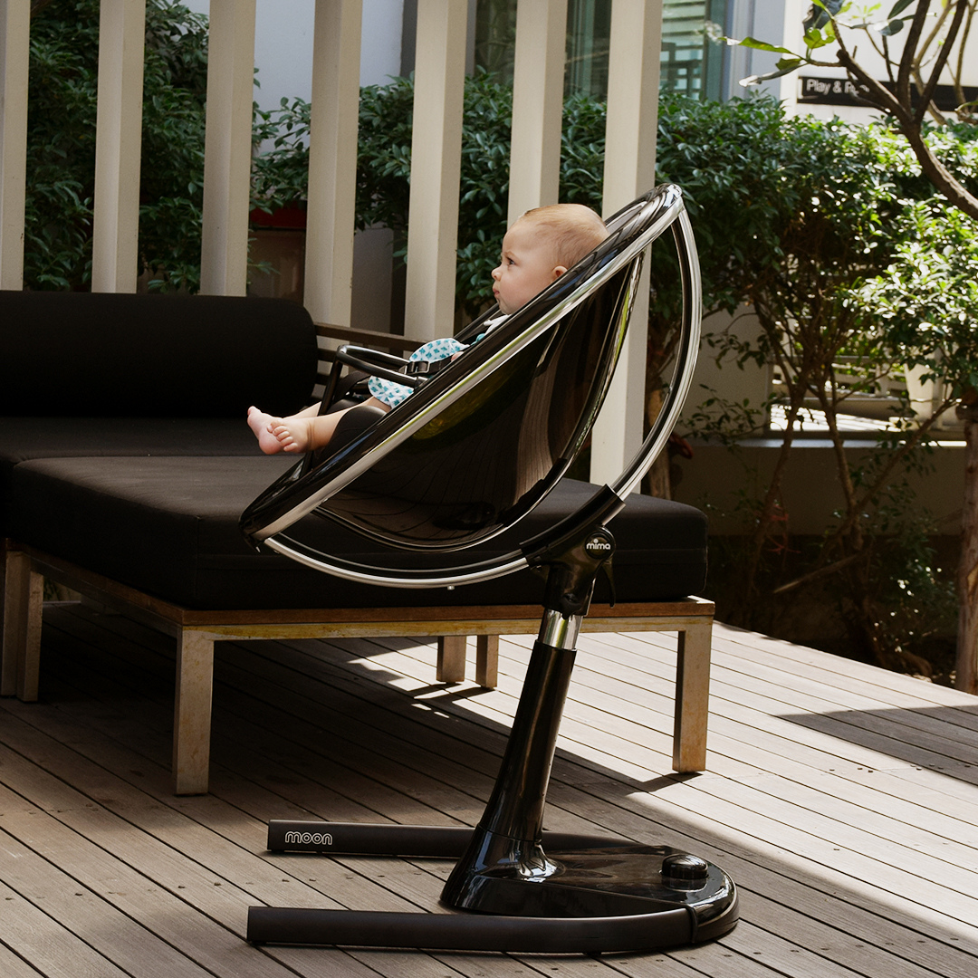 Baby in living room with sleek Moon high chair in black.