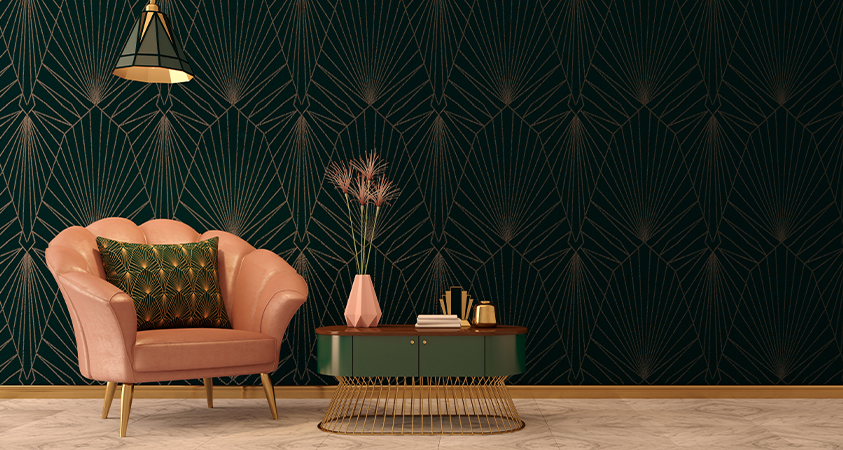 A simple Art Deco style living space with a pink clamshell armchair and a green wood and metal coffee table. The wallpaper features a simple black and gold repeated pattern with sharp, fine lines, and the armchair features a matching throw pillow in gold and green.