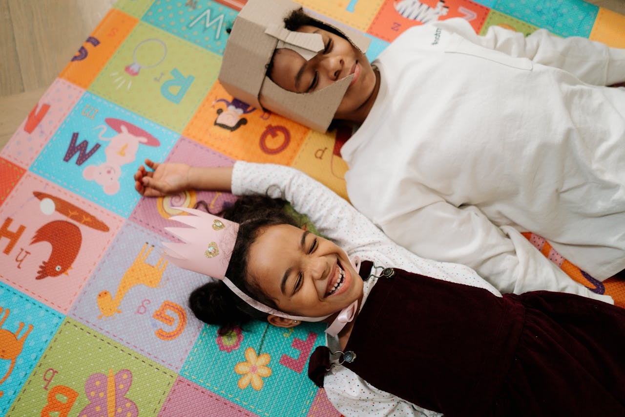 Two kids lying down on a colourful mat.