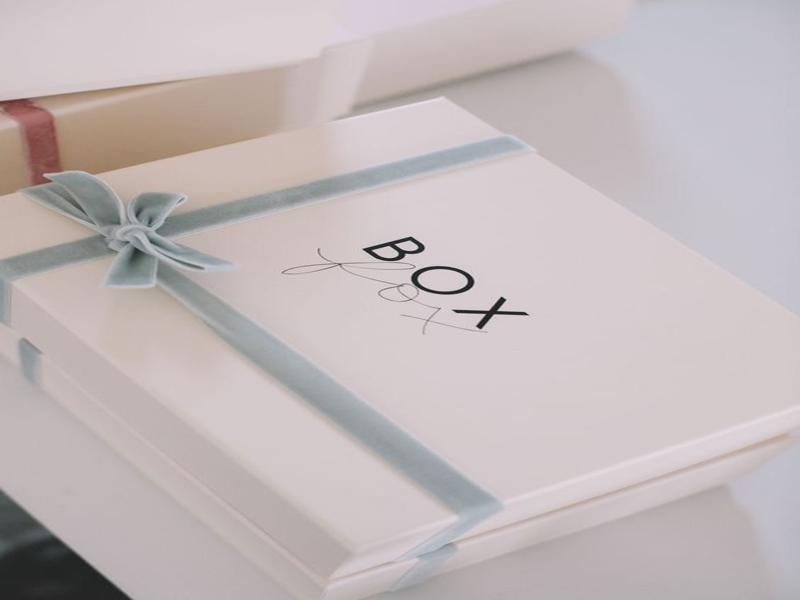 A picture of a white subscription box wrapped with a soft blue ribbon and bow, with the word “BOX” printed on the lid.