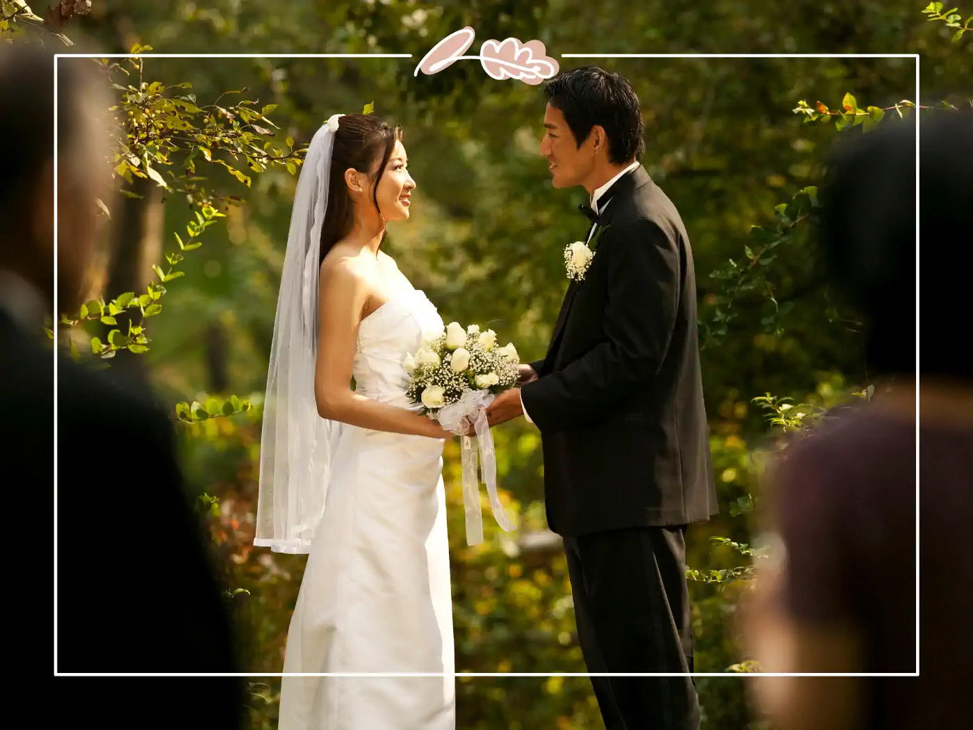 A bride and groom standing together outdoors, holding hands and gazing lovingly at each other. Fabulous Flowers and Gifts.