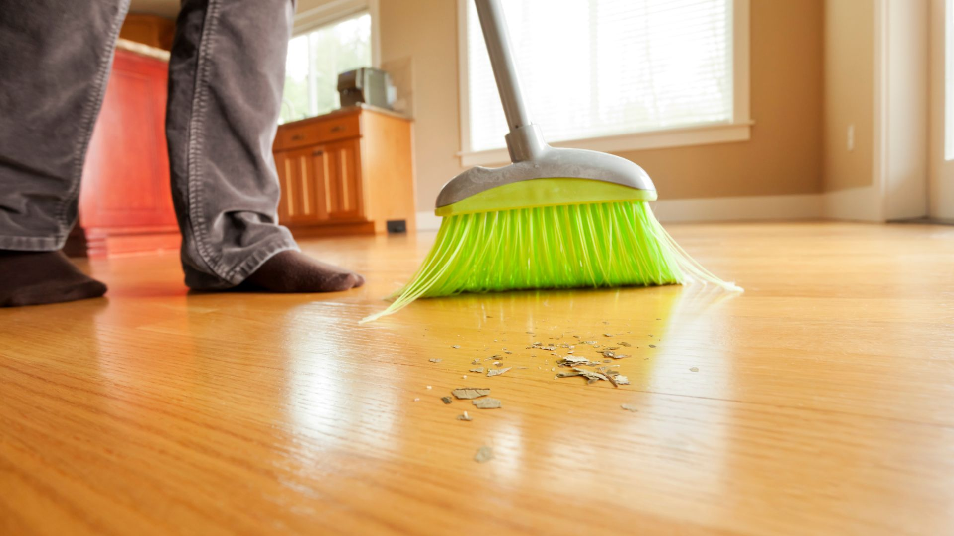 An image of a person sweeping their hardwood floor with a broom to prevent pests.