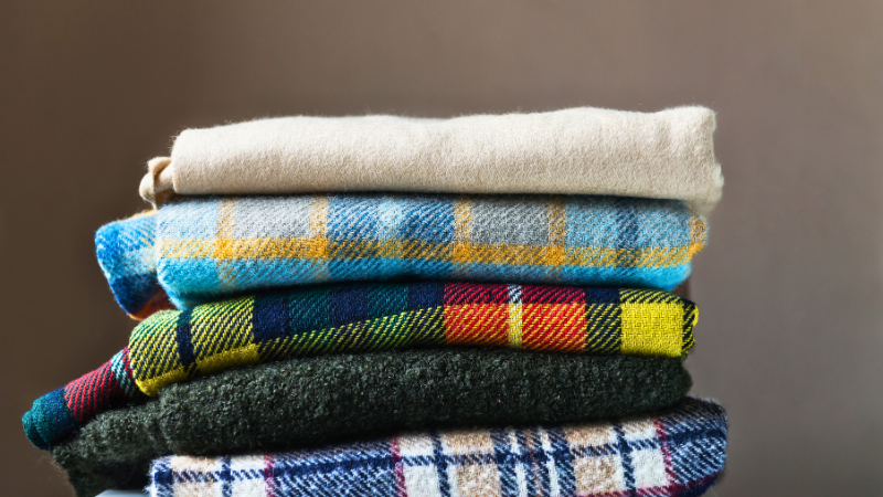 A stack of folded cotton blankets sitting on top of a wooden table