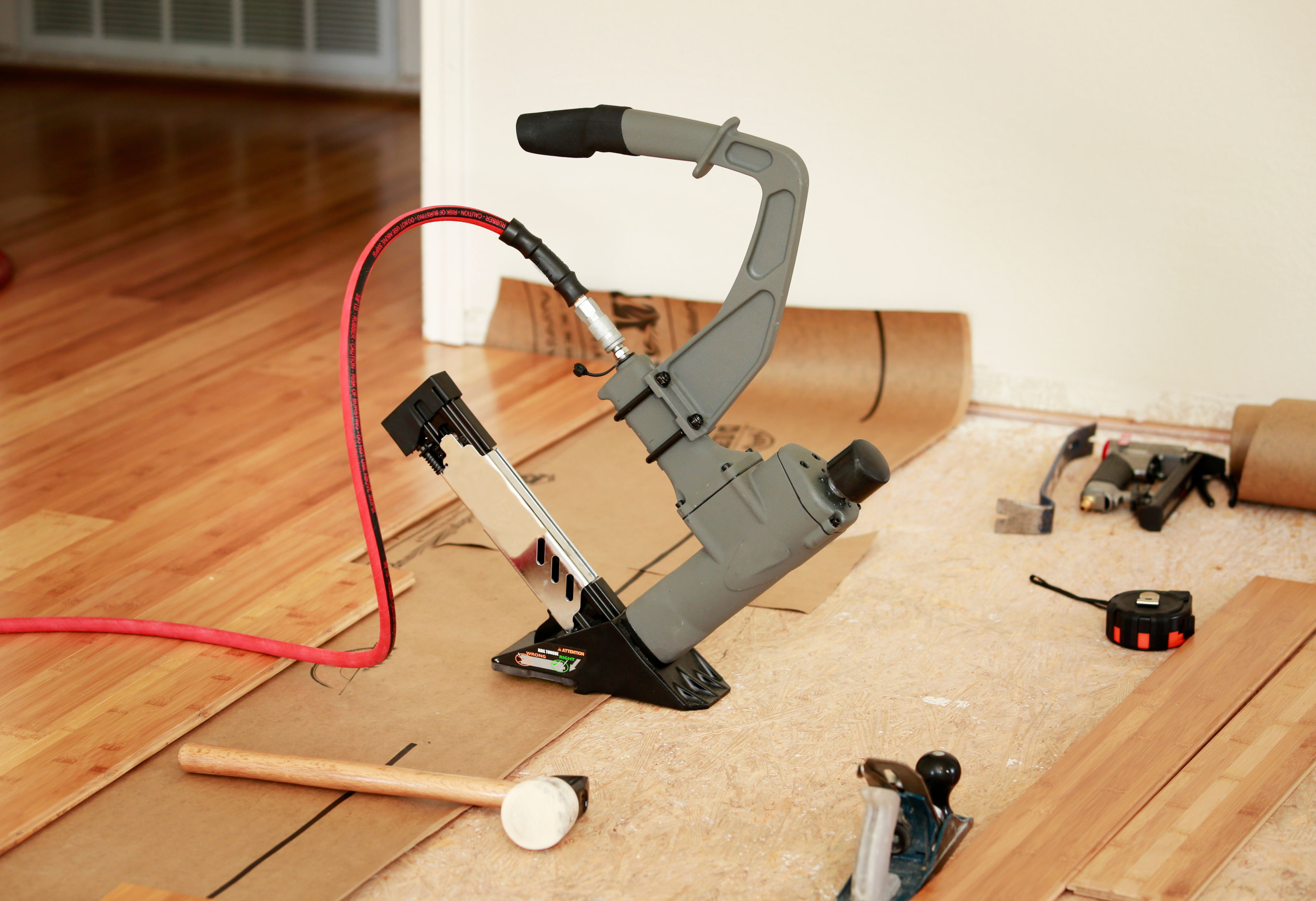 A flooring nail gun placed on a wooden floor with some unfinished bamboo planks.