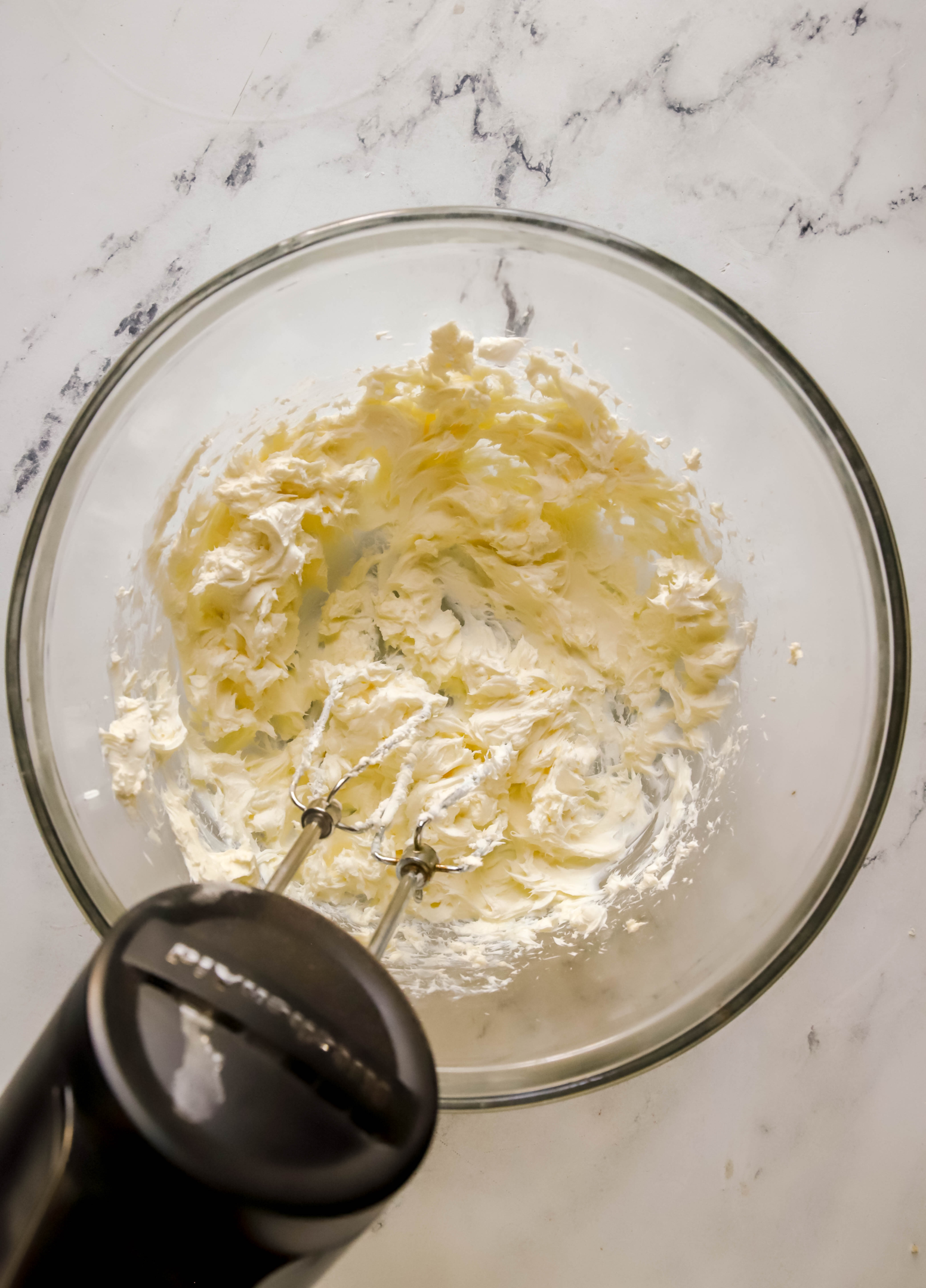 hand mixer mixing a glass bowl of cream cheese and butter