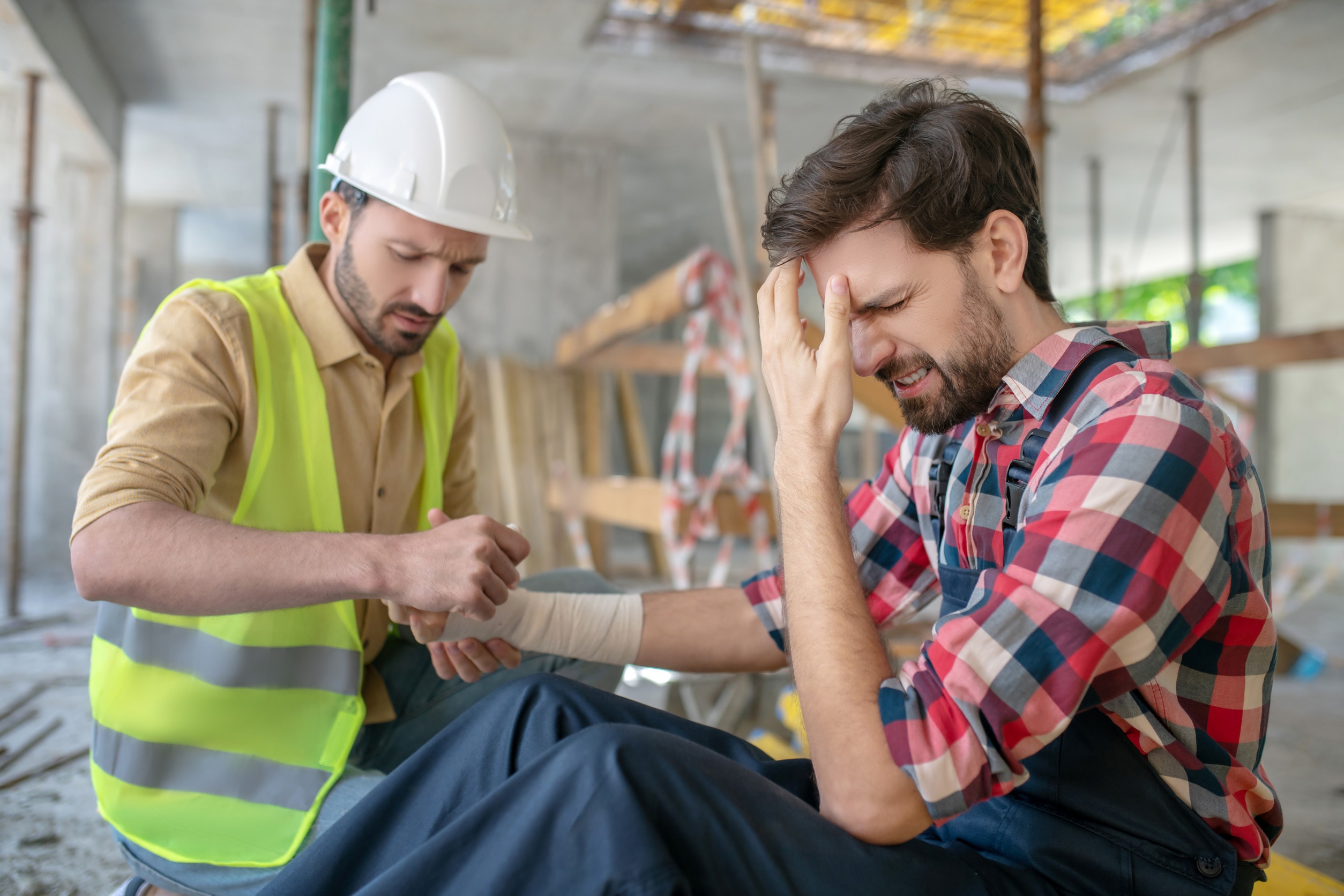 A worker performs first aid on a colleague who suffered construction site injuries