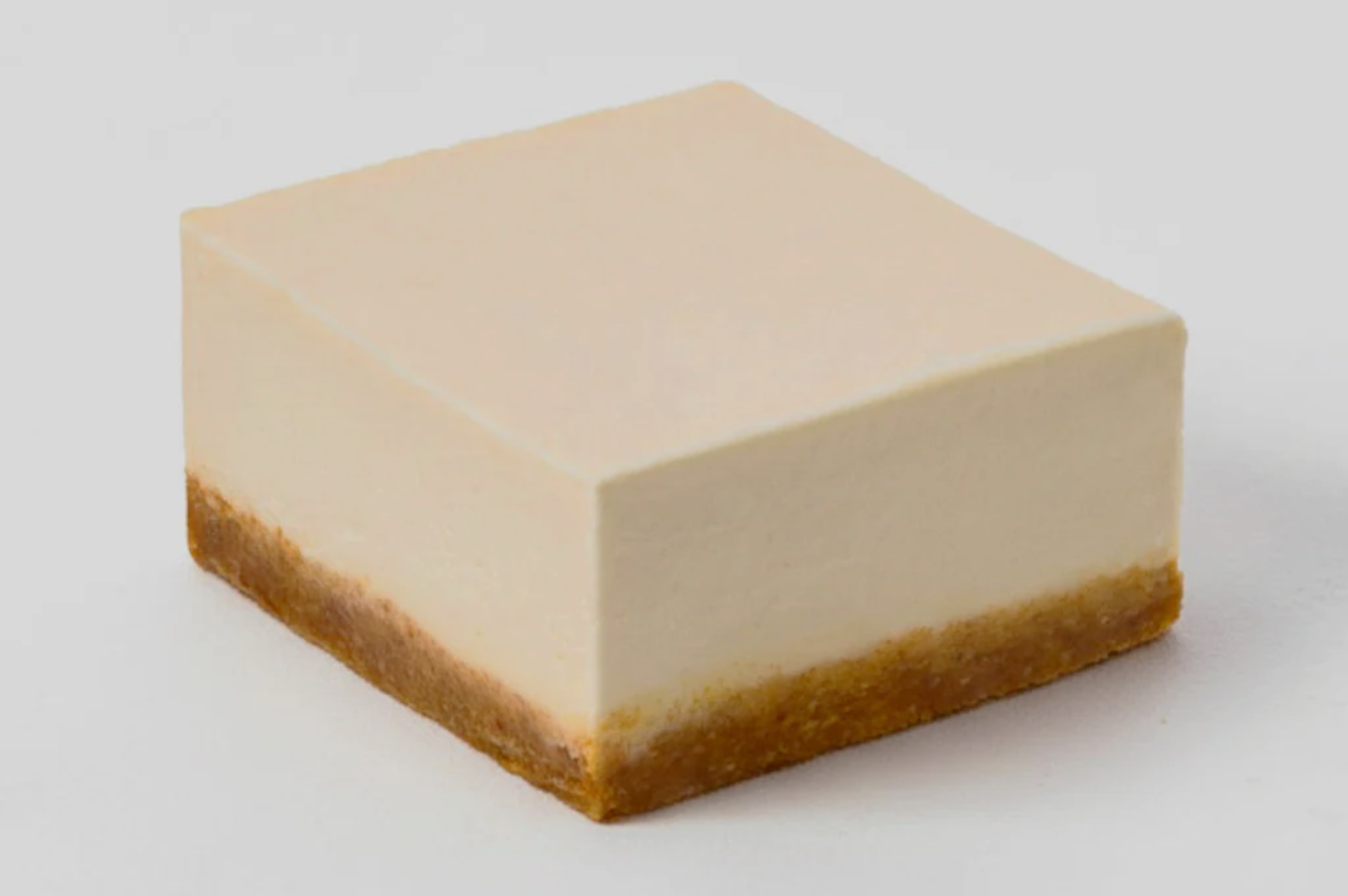 A smooth, square cheesecake slice with a creamy, pale top layer and a brown graham cracker crust, set against a simple white background.