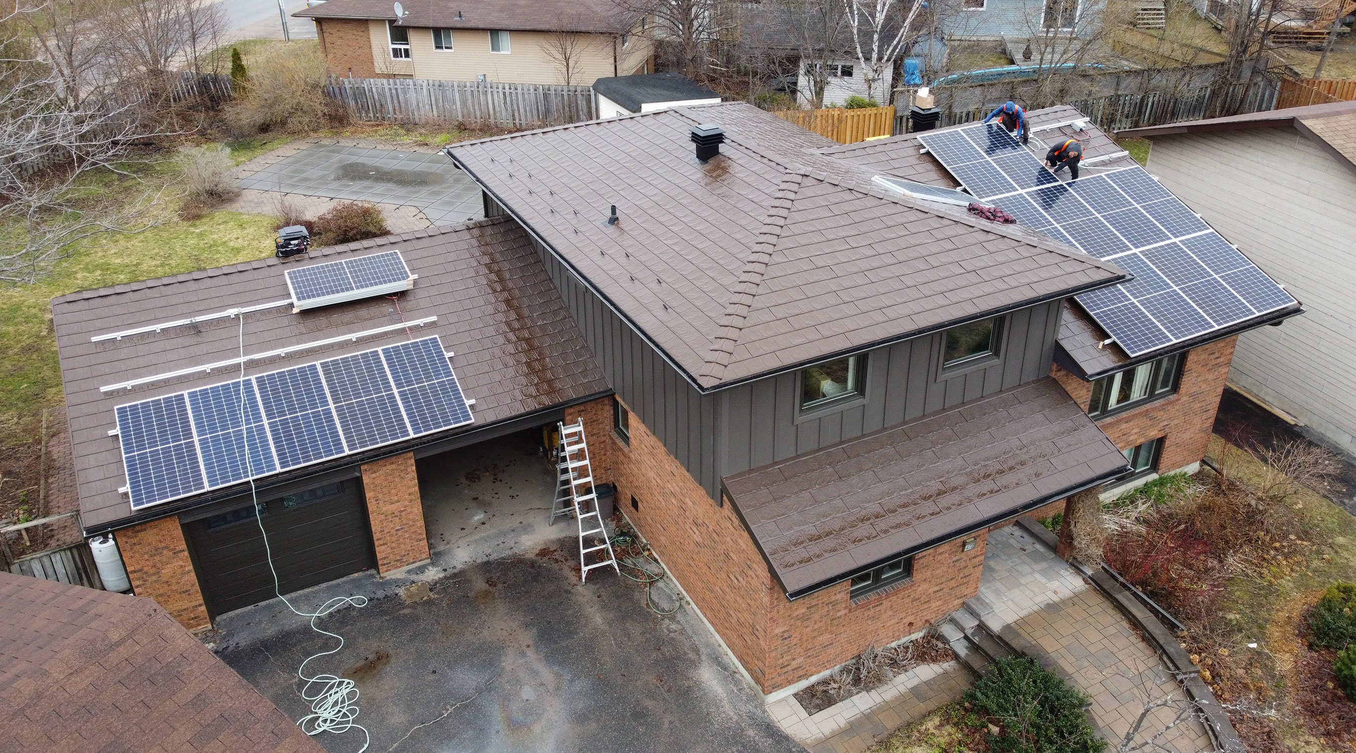 An aerial view of a house, highlighting Roof Pros Plus steel shingles with solar panels for better energy efficiency.