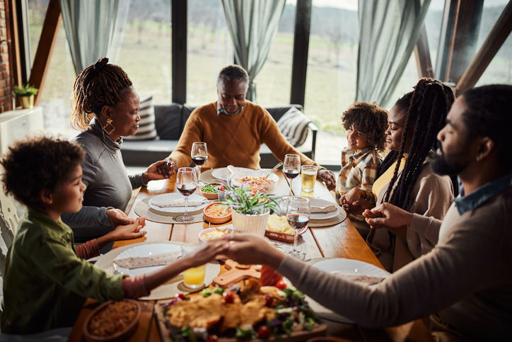 An African American family gathered around the table saying grace. 