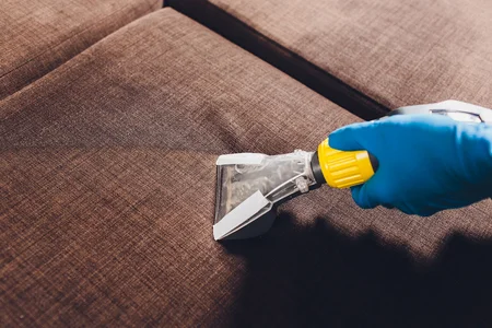 Professional deep cleaning a brown tufted sofa with an upholstery cleaner by Cleanology SG, showcasing expert sofa cleaning services to remove dirt and stains for a pristine finish in Singapore.