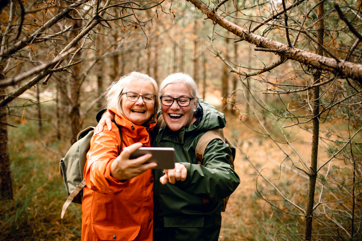Two mature women hiking and stopping to snap a selfie.