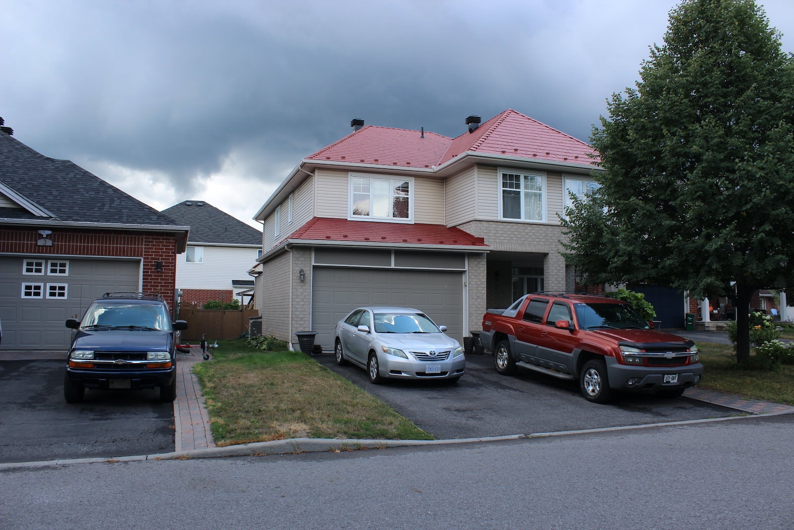 A picture of a home in a neighbourhood with a vibrant red roof and a truck and a car in the driveway.