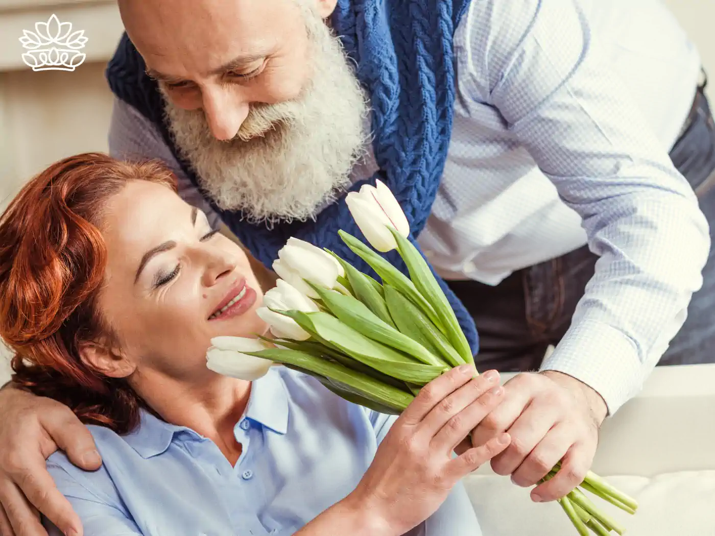 An older man with a beard surprises a delighted woman with a bouquet of fresh white tulips, showcasing affection and happiness. Fabulous Flowers and Gifts delivered with heart. Valentine's Day Flowers.