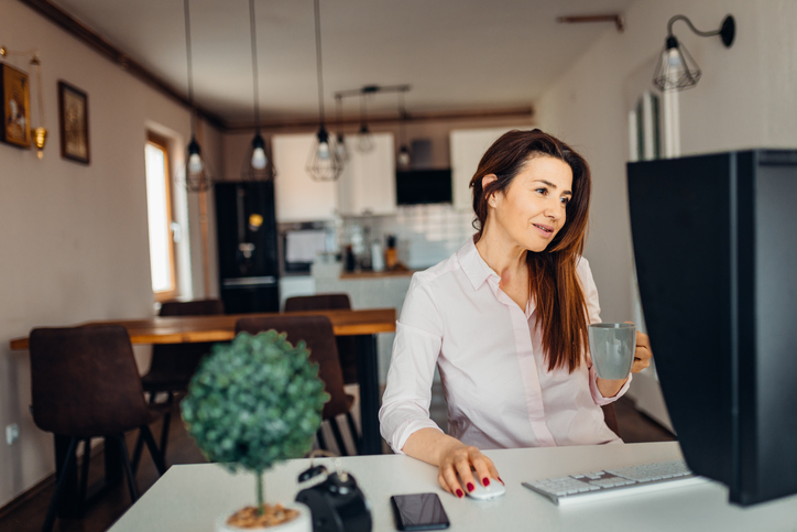 Brunette woman drinking coffee and working on her computer.