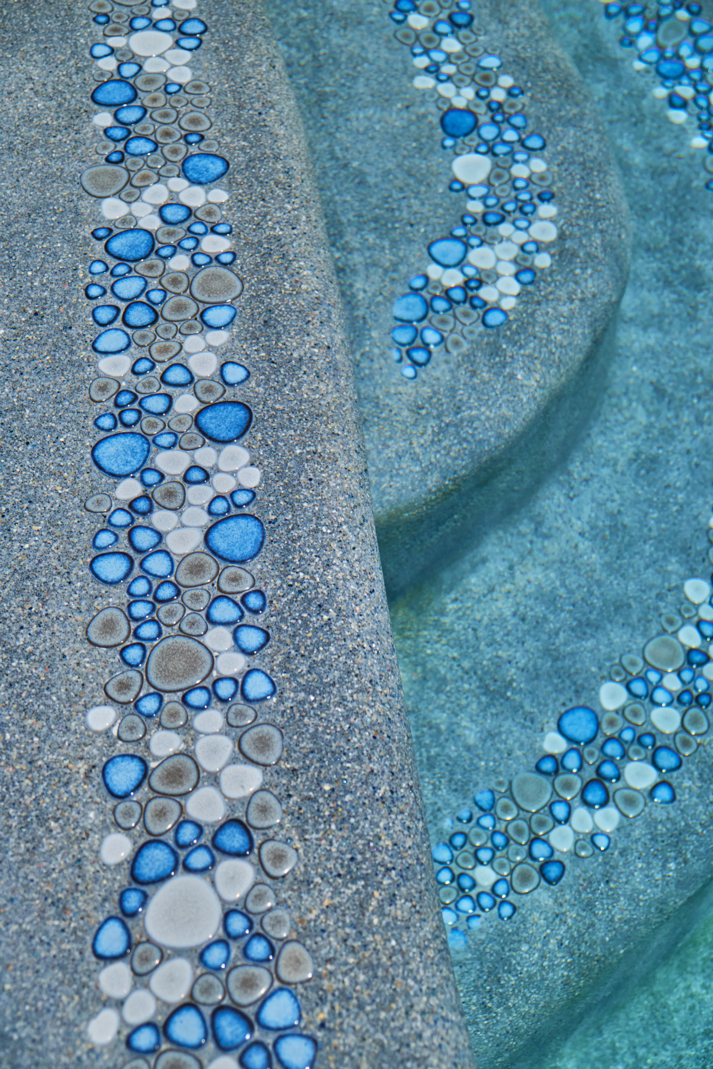 Steps in a swimming pool with tile accent detail and pebble surface.