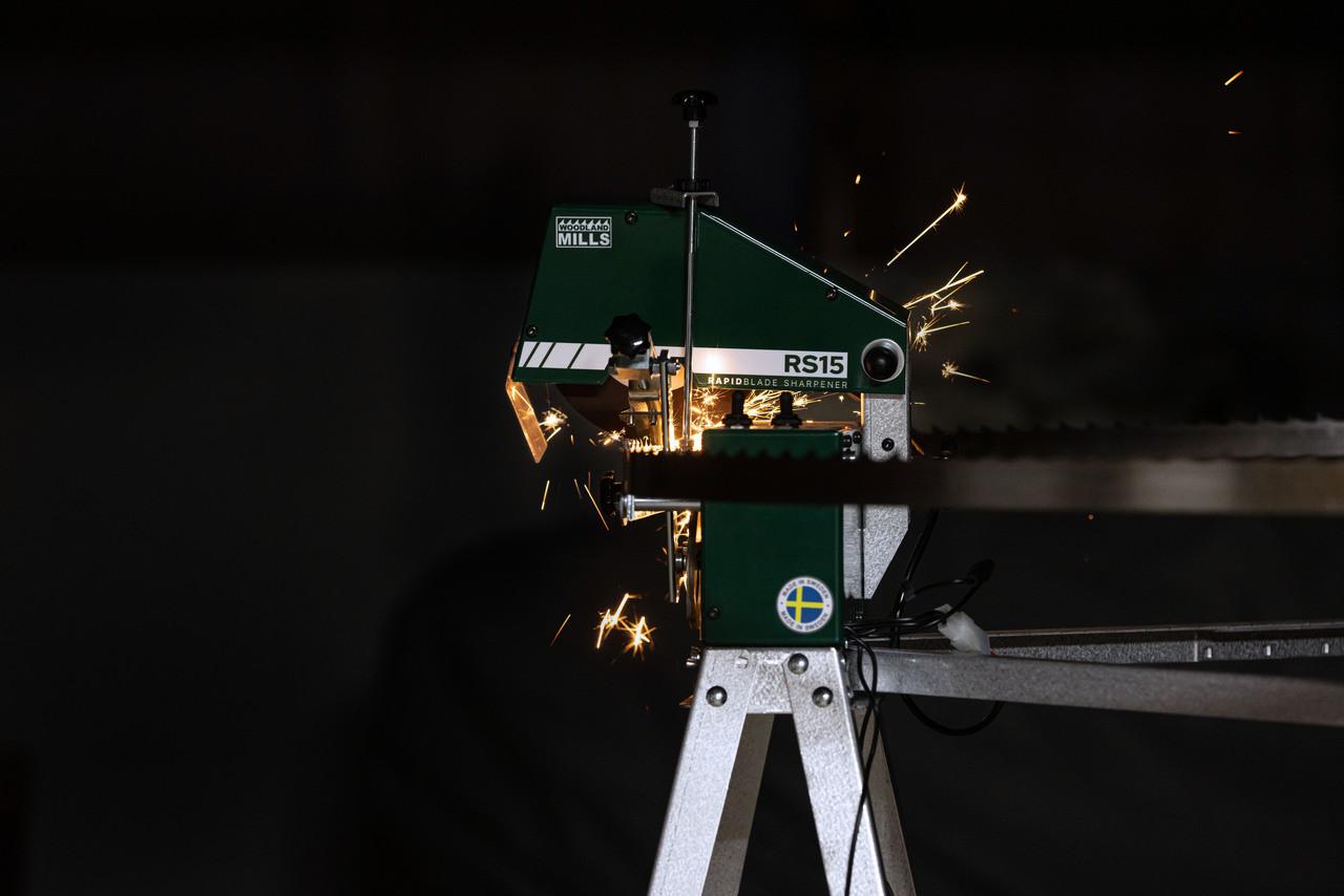 A Woodland Mills RS15 Bandsaw Blade Sharpener in a dark room sharpening a sawmill blade.