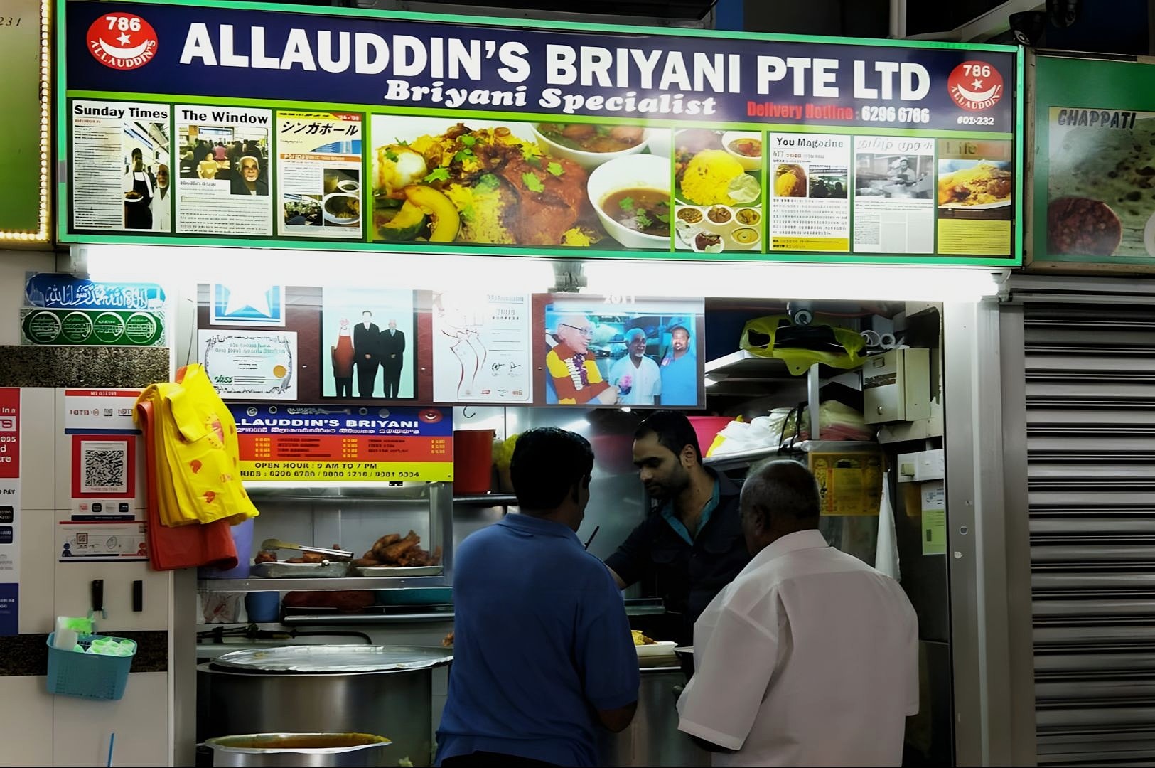 A bustling biryani food stall at a hawker center with a colorful sign above. Two customers are being served by a vendor, creating a lively atmosphere.