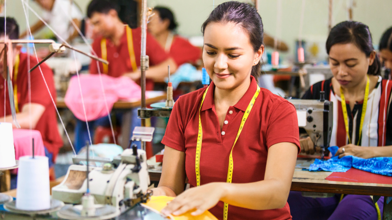 A lady in a red shirt is working on fabric on a sewing machine