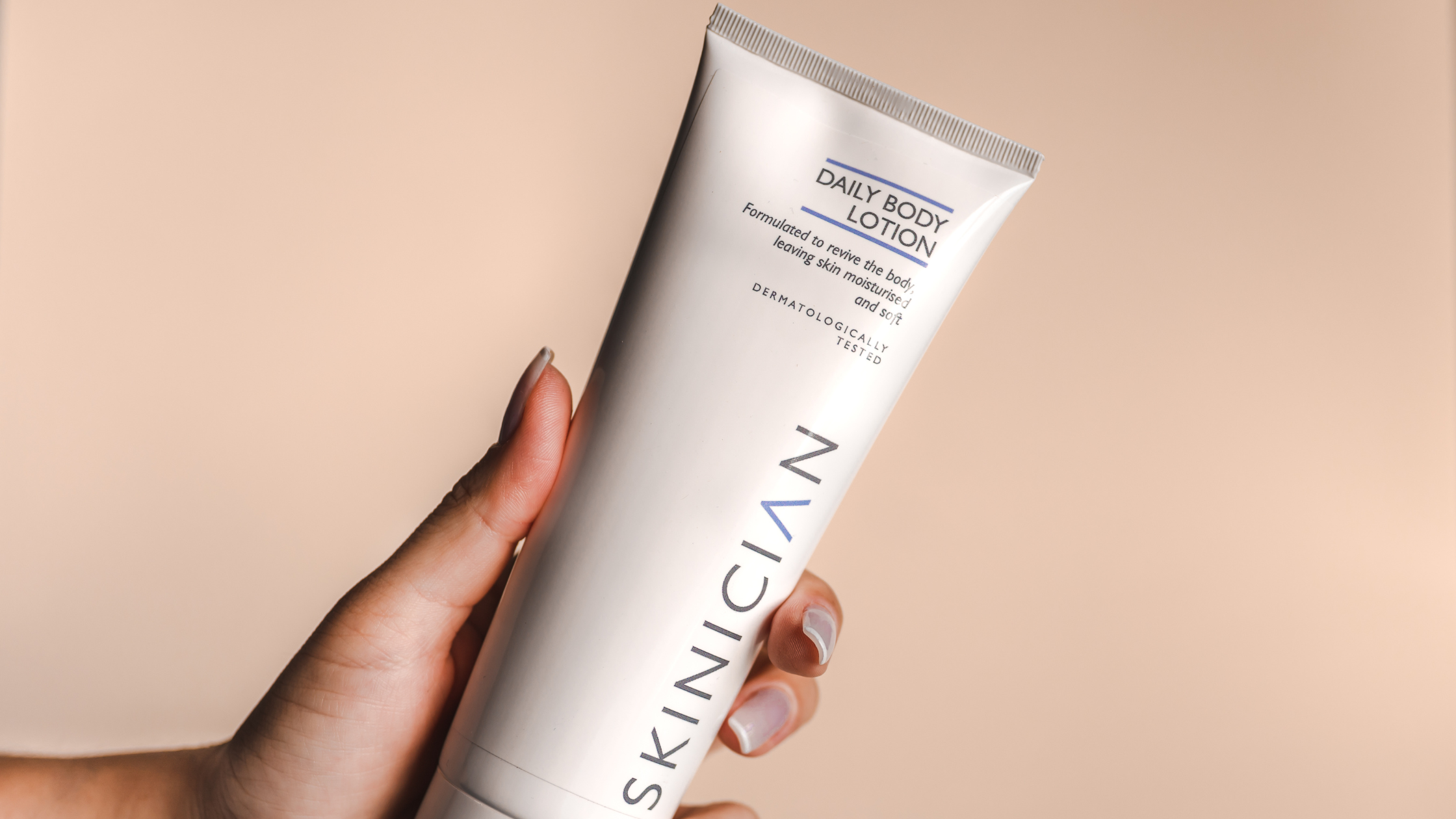 A bottle of SKINICIAN Daily Body Lotion, a lotion ideal for caring for menopausal skin, held in a hand against a neutral background.
