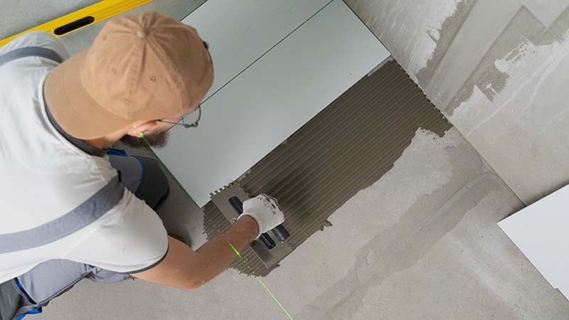A man installing white porcelain tiles on the floor