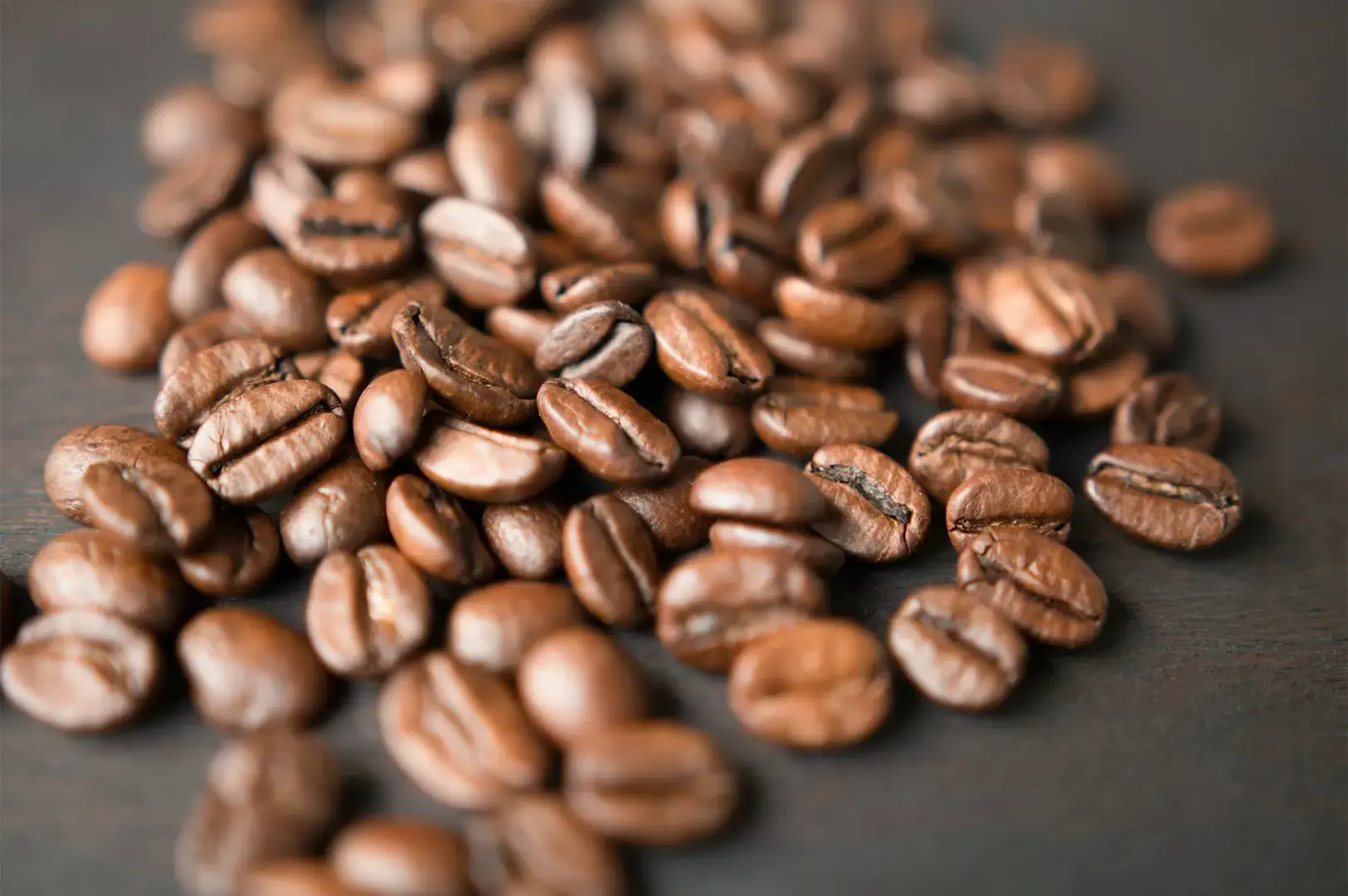 Coffee beans scattered on a smooth black surface.