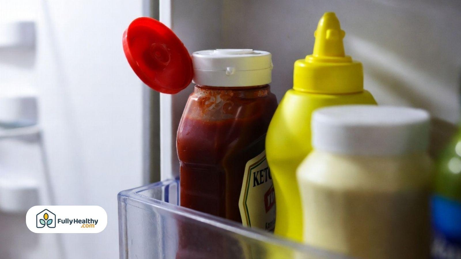 Opened ketchup bottle stored in refrigerator door beside condiments.