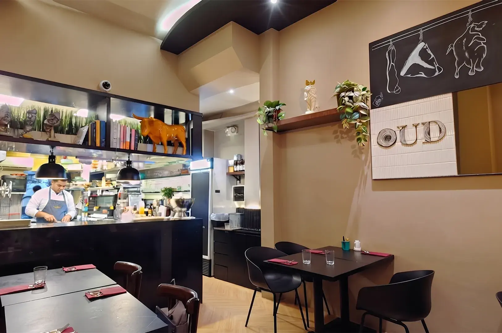 Modern restaurant interior with a chef working in an open kitchen, tables set for dining, and decorative wall art.