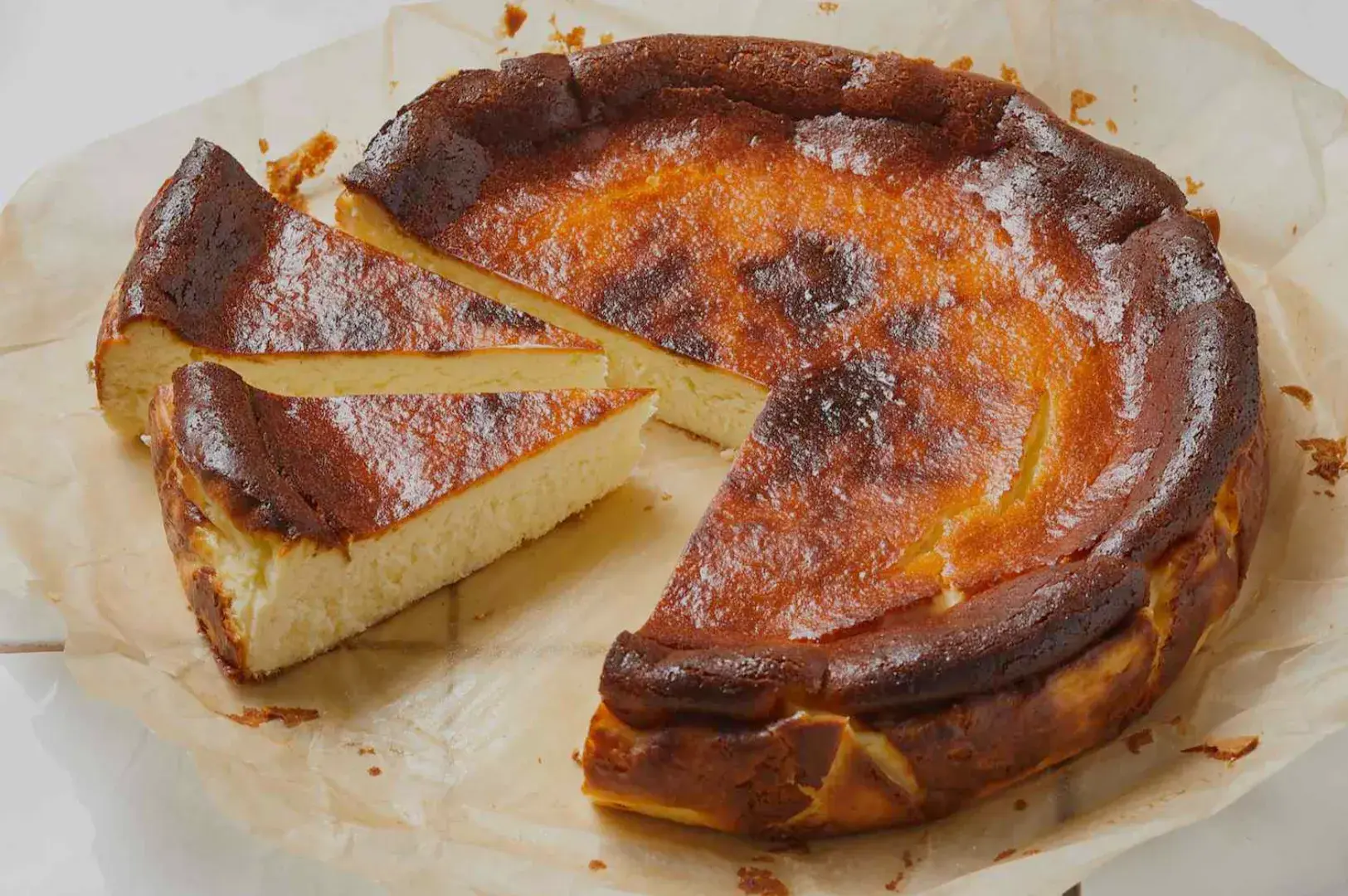 A partially sliced basque burnt cheesecake on parchment paper with a golden-brown crust.