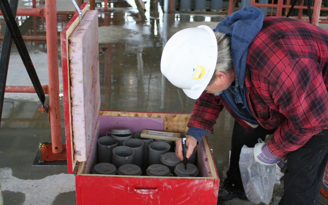 A technician handling and curing a concrete cylinder test specimen