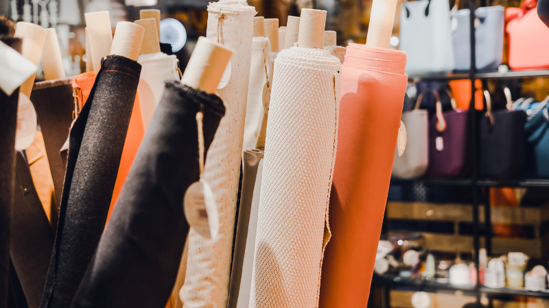 Rolls of fabric in various colors are displayed on a rack in a store.