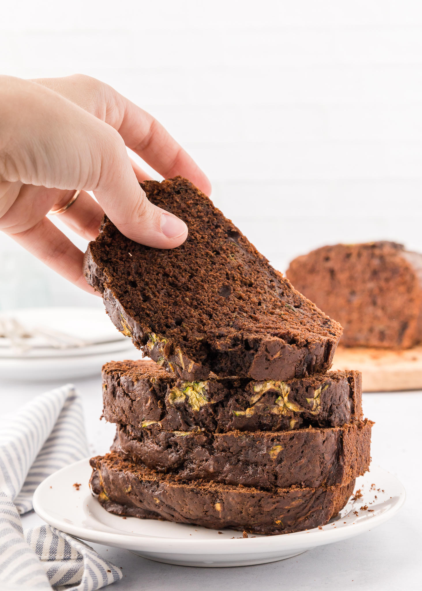 hand removing a slice of chocolate zucchini bread from a stack of slices