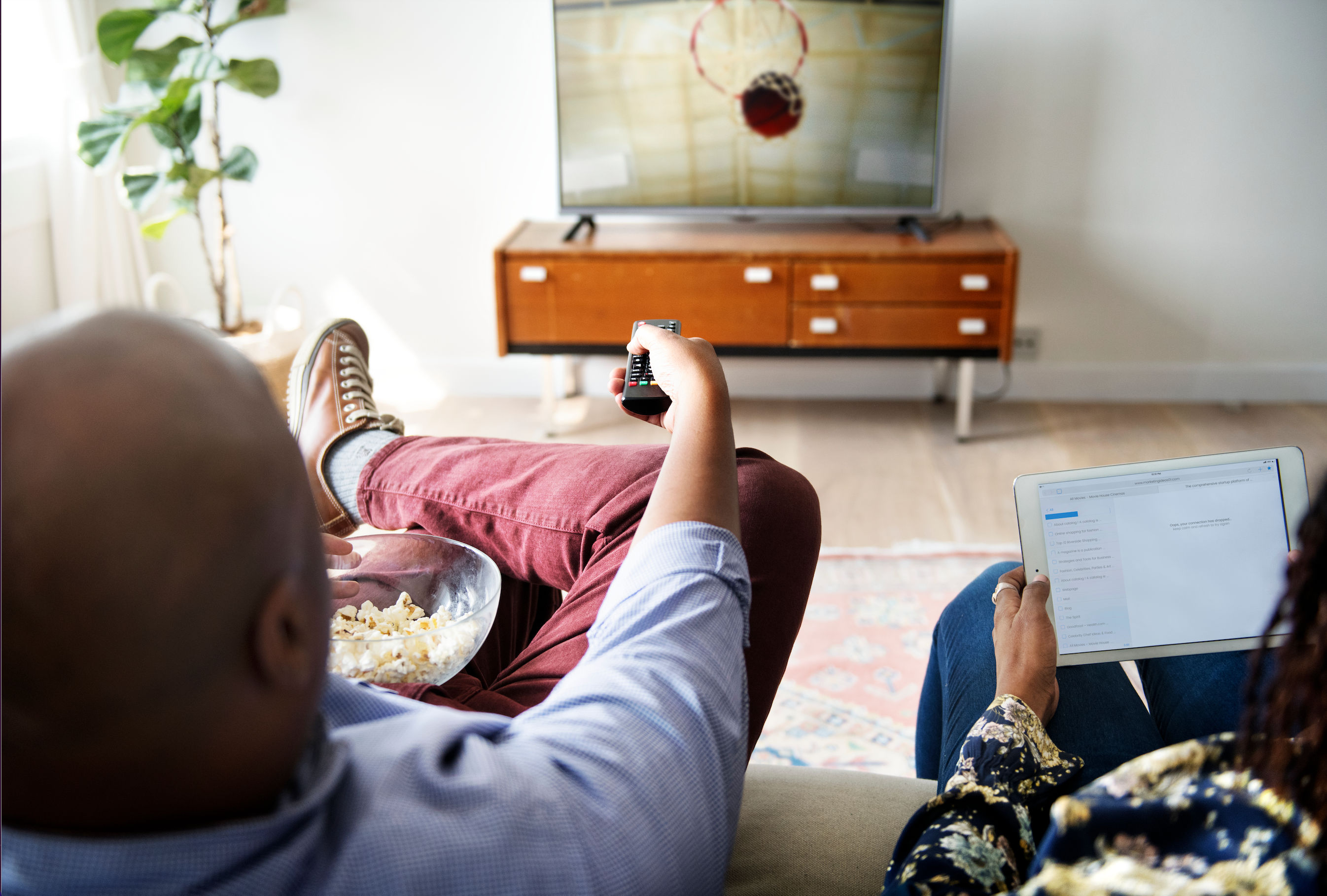 a man and woman watch tv in the living room while she browses her tablet