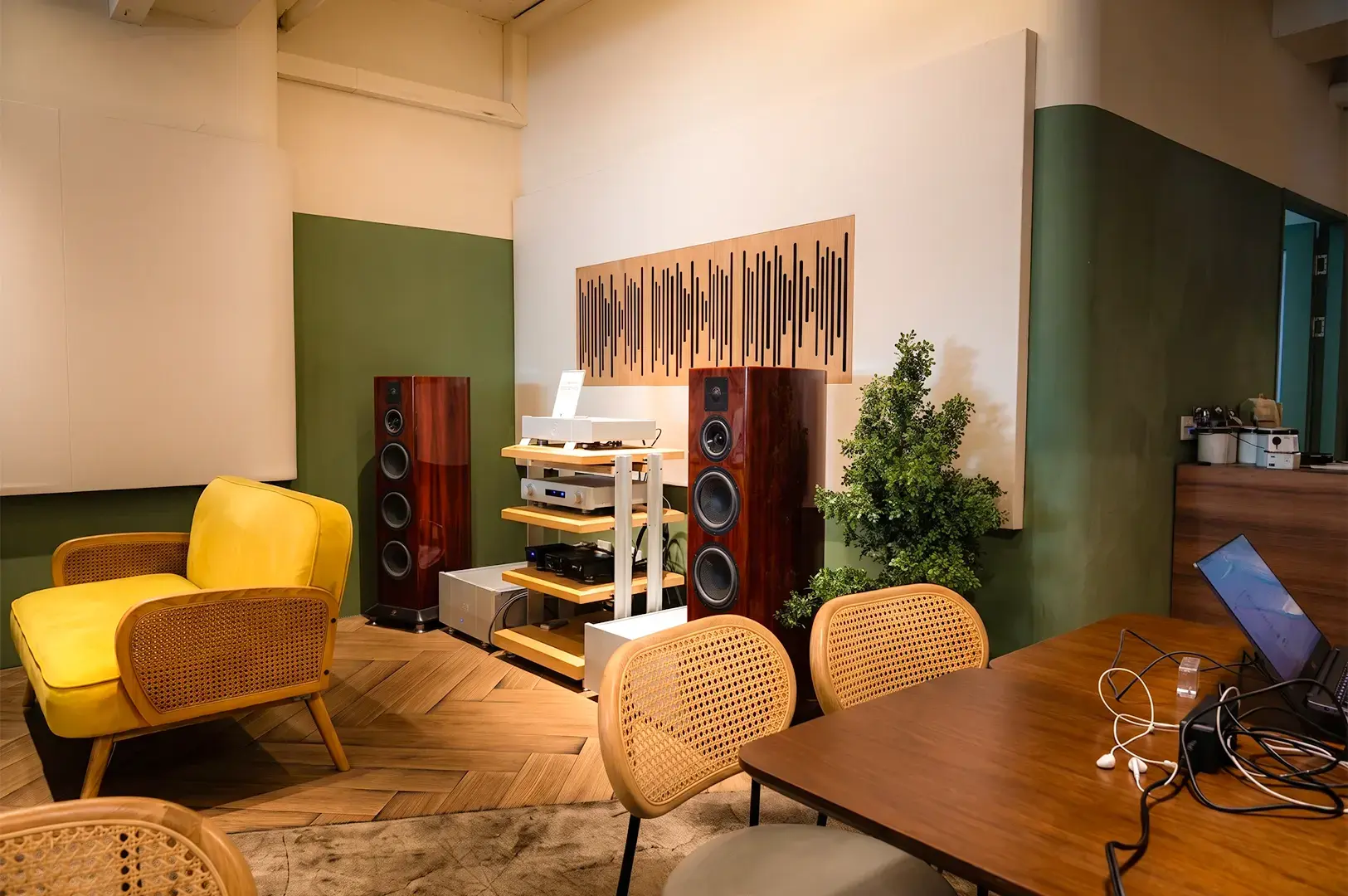 A wide angle view inside Acoustics Coffee Bar, its brown, white, and green colored furniture and decorations giving a warm cozy vibe and an artistic flare with the music themed displays of speakers and sound waves.