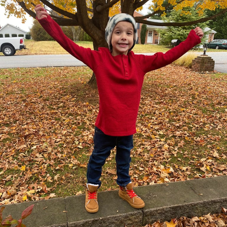 Brandi's son wearing a winter outfit composed of boots, jeans, a long sleeve tee, and beanie.