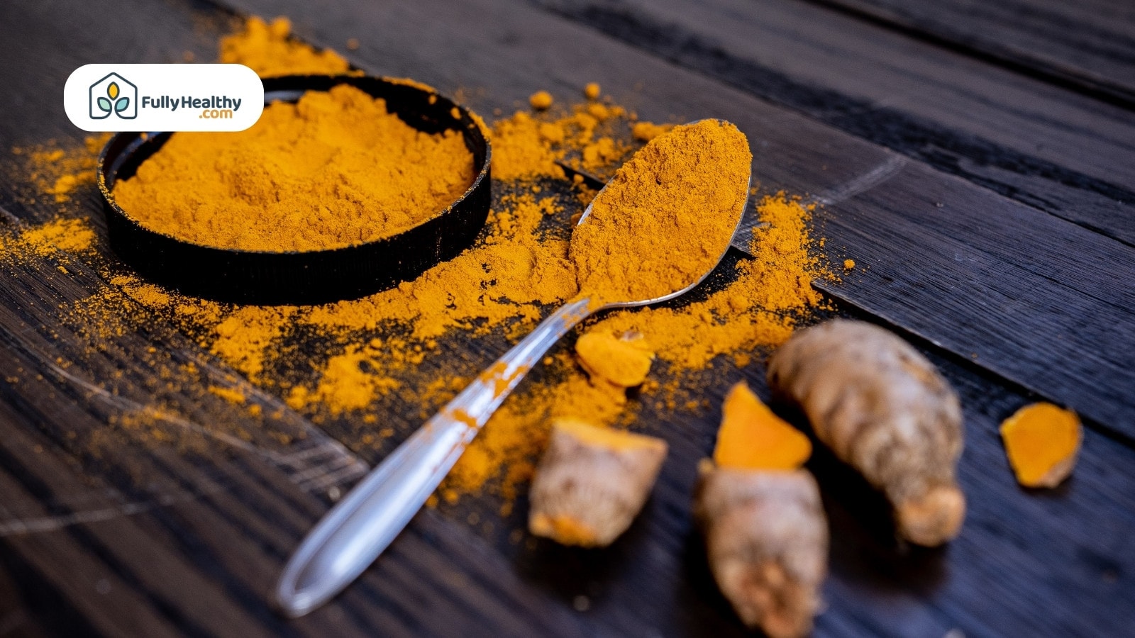 Turmeric powder in spoon with fresh roots on wooden surface