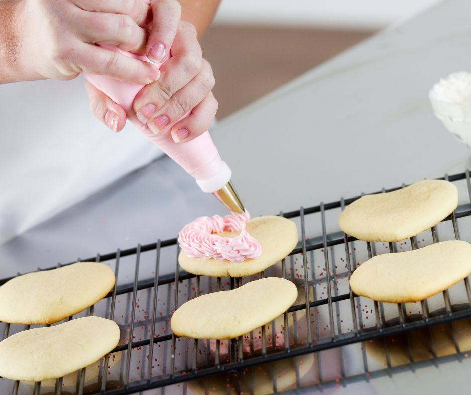 heart cookies being frosted with a pink frosting in a piping bag 