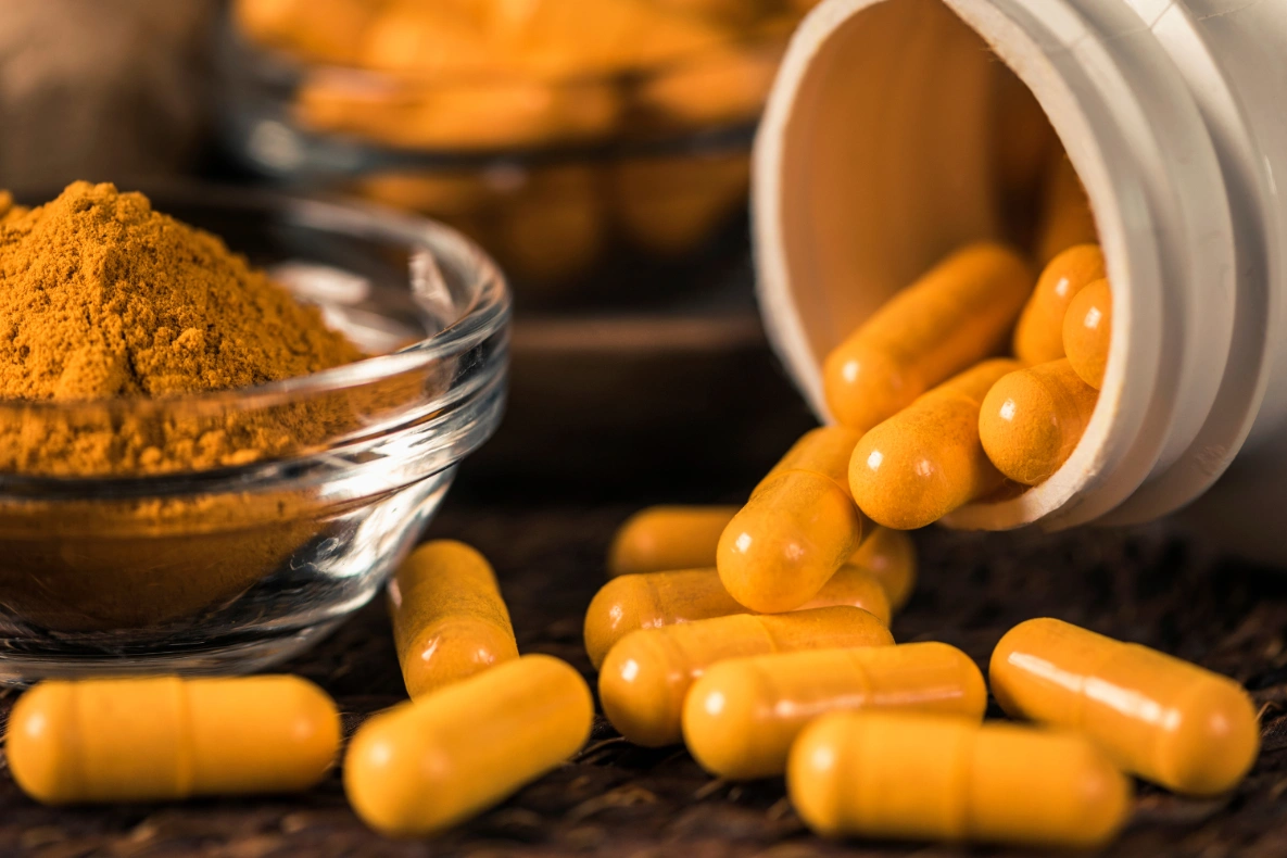 A white bottle of yellow capsules next to a glass bowl of yellow powder.