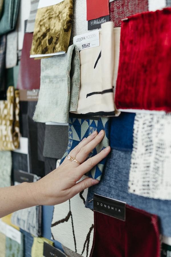 Close-up of a designer’s hand touching fabric swatches on a material sample wall.
