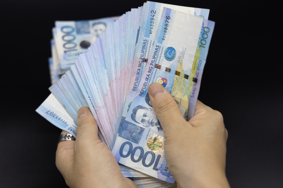 Hand holding a fan of Philippine peso bills representing salary expectations in the Philippines