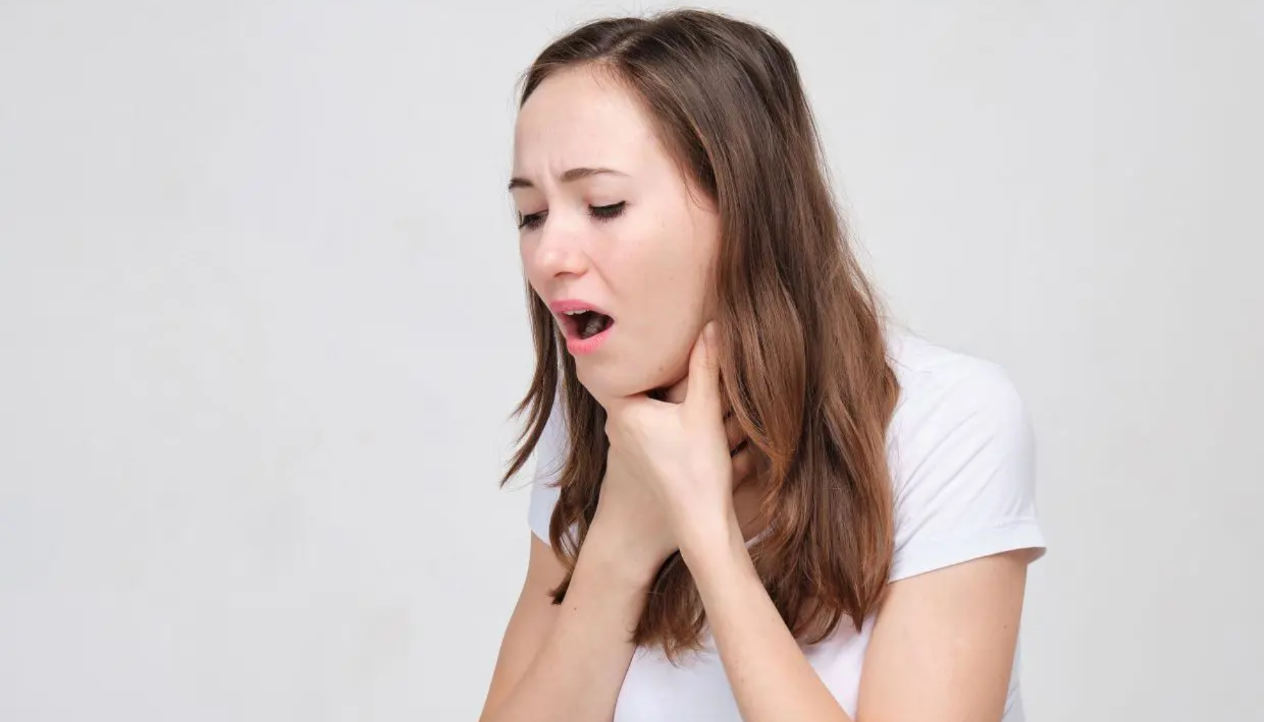 Kvinne i hvit t-skjorte holder seg til halsen og ser ut til å ha problemer med å svelge.