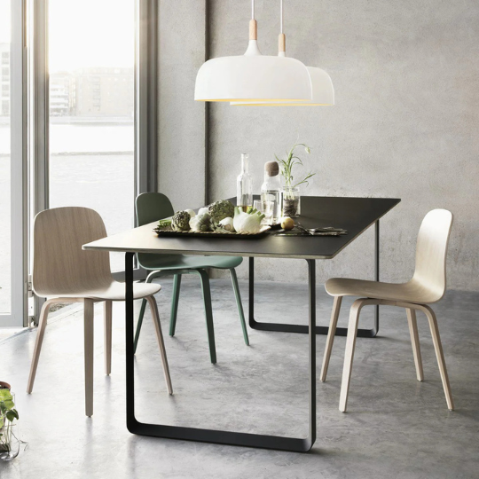 Modern dining room with minimalist black table, mix of wooden chairs, and two white pendant lights hanging above, styled with natural décor.