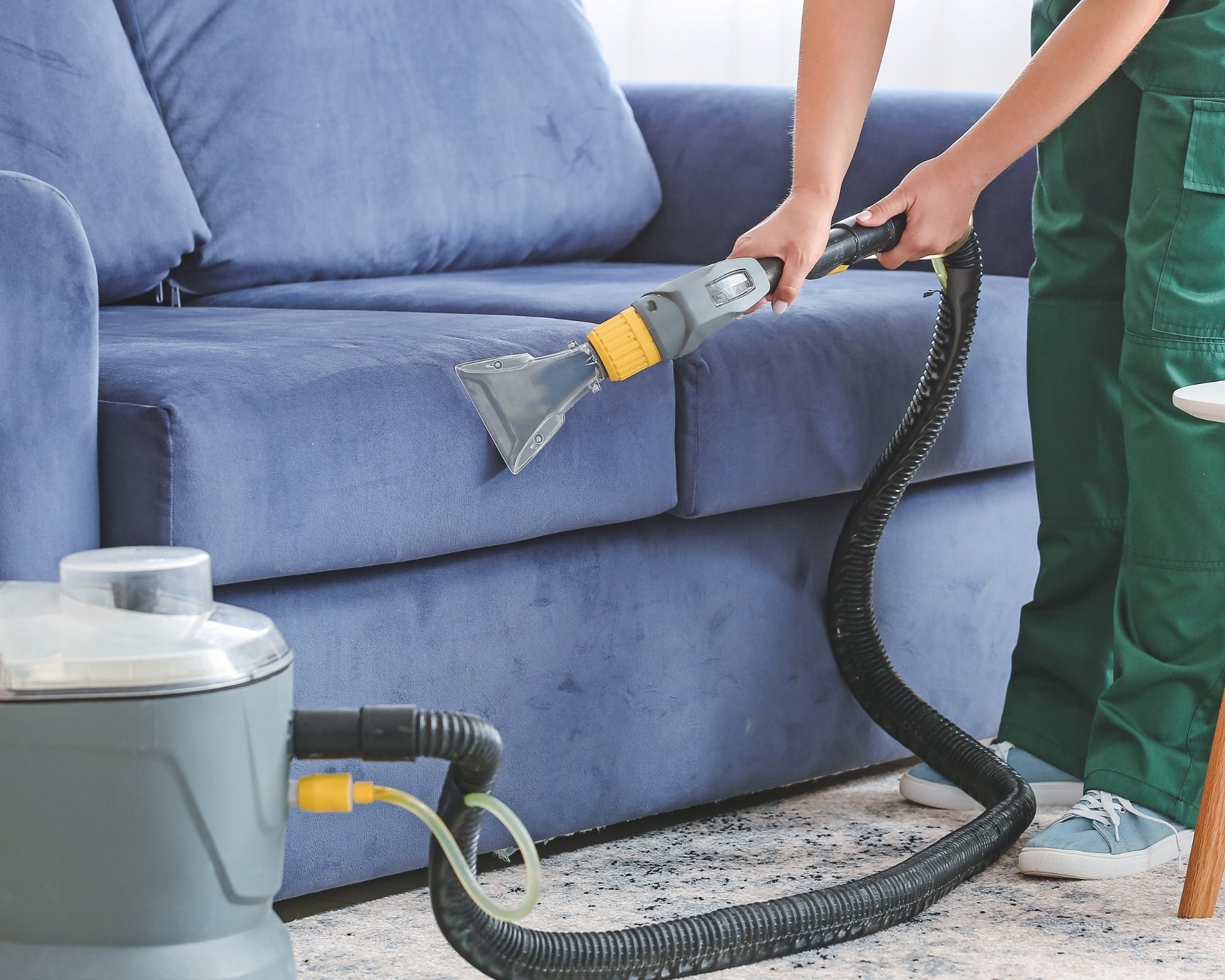 Professional upholstery cleaning on a beige sofa with a cleaning tool and brush, highlighting detailed sofa cleaning services to restore fabric furniture to its original condition.