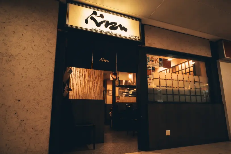 The entrance of Kazu Sumi-yaki Restaurant (unit 04-05) at Cuppage Plaza, showing a traditional black noren curtain under a stylized backlit calligraphy sign.
